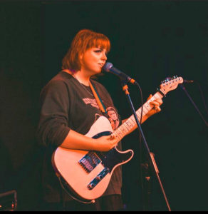 Young woman at Brighton Youth Centre playing the guitar in the music room and performance stage