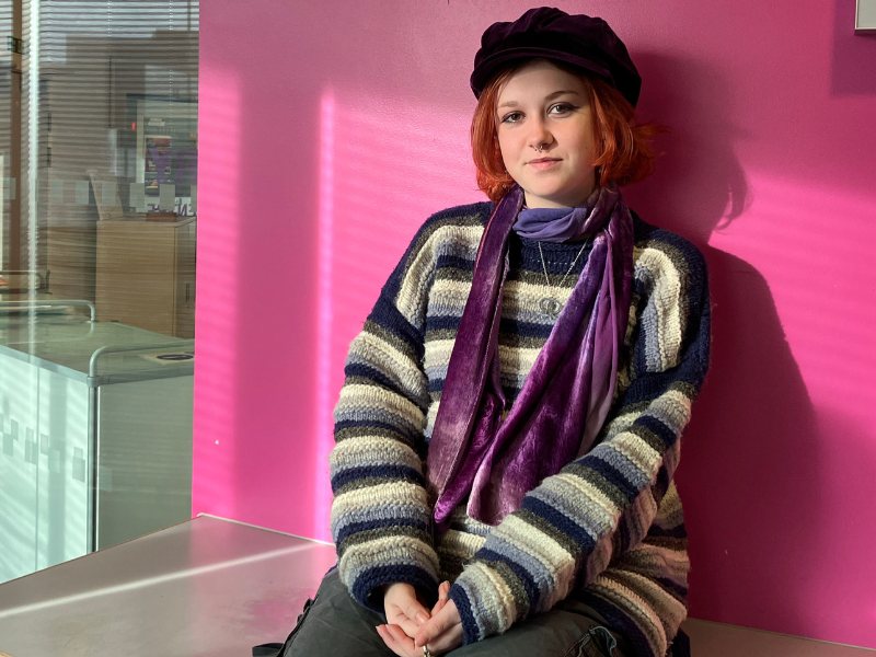 Young woman called Tean sitting by colourful pink wall.