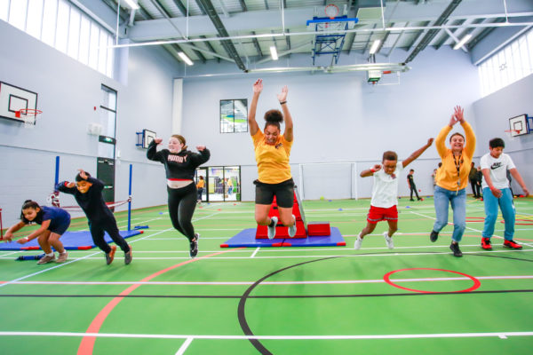 Group of young people jumping, stretching and leaping in a sports hall at an Onside youth Zone.