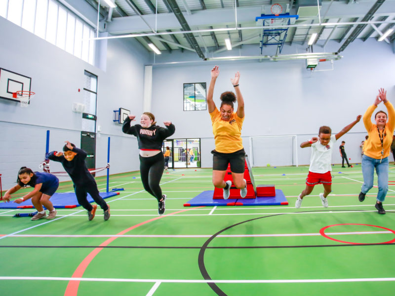 Group of young people jumping, stretching and leaping in a sports hall at an Onside youth Zone.