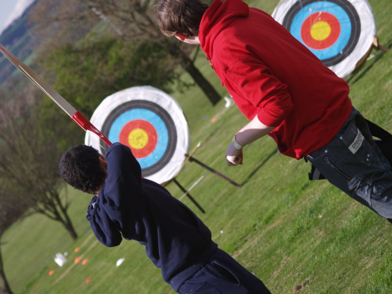 Two young people enjoying archery at Bentley Air Scouts. One young person is pulling back the bow ready to hit the target in front of them.