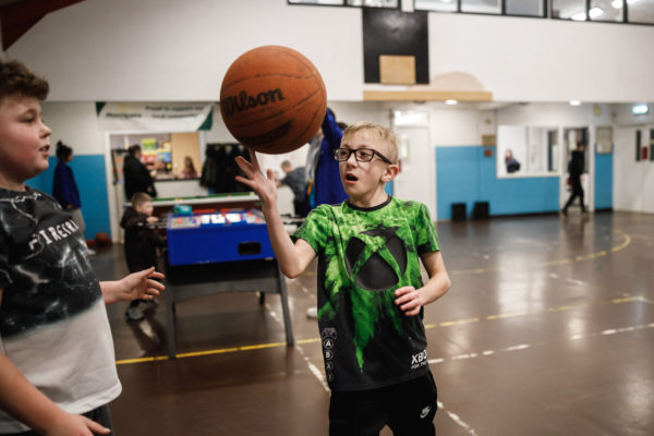 Two young people are practising basket ball skills at Burnley Boys and Girls Club. One young man is balancing the ball on his finger and watched by another young person.