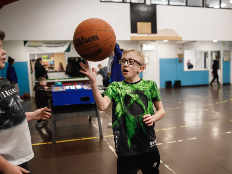 Two young people are practising basket ball skills at Burnley Boys and Girls Club. One young man is balancing the ball on his finger and watched by another young person.