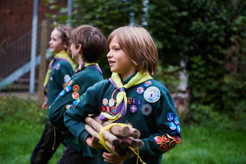 Three young Scouts carrying wood in the woodland setting of their Scout hut in Norwich