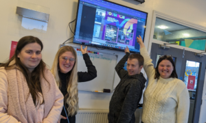 Young people are smiling and pointing at a screen showing the colourful new branding for AutismAble's youth hub