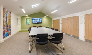 Larage Scout meeting room, with table and chairs. The space includes a large TV screen and images of scouts on the walls.