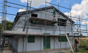 Building work in progress on the new Hoveton and Wroxham Scout Hut. Scaffolding is up and people are working on the ground and towards the roof apex.